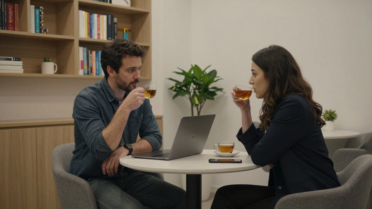 A man and woman having a quiet tea in a neutral co-working lounge, books and plant between them.