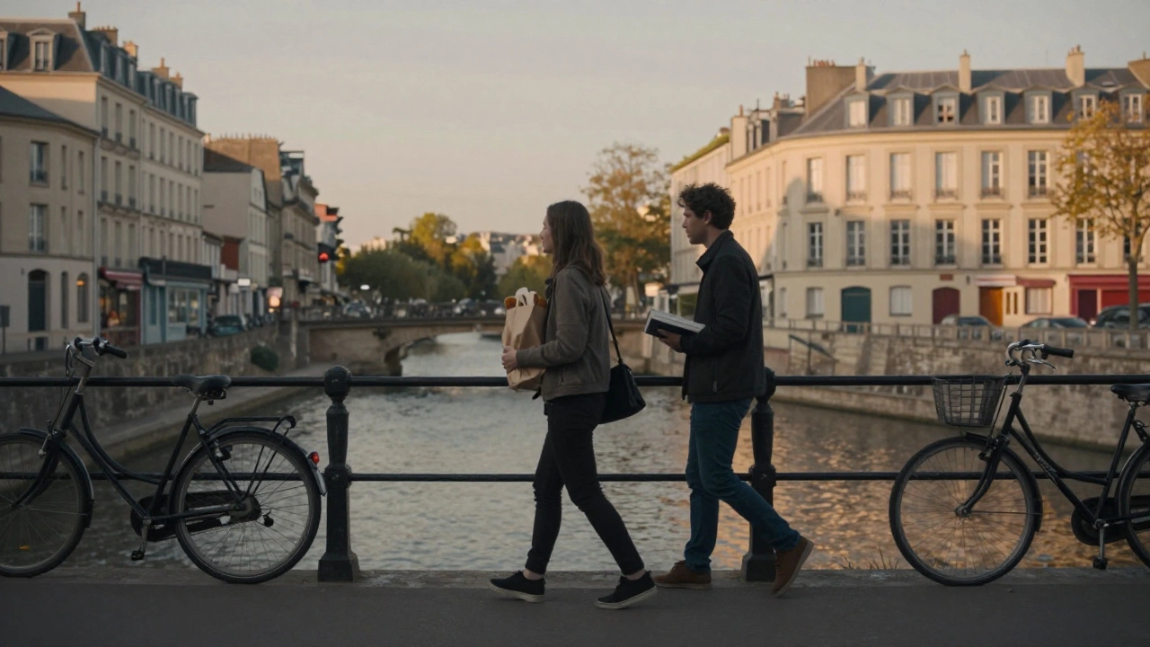 Two people walking calmly along a Paris canal at sunset, books and bakery bag in hand.